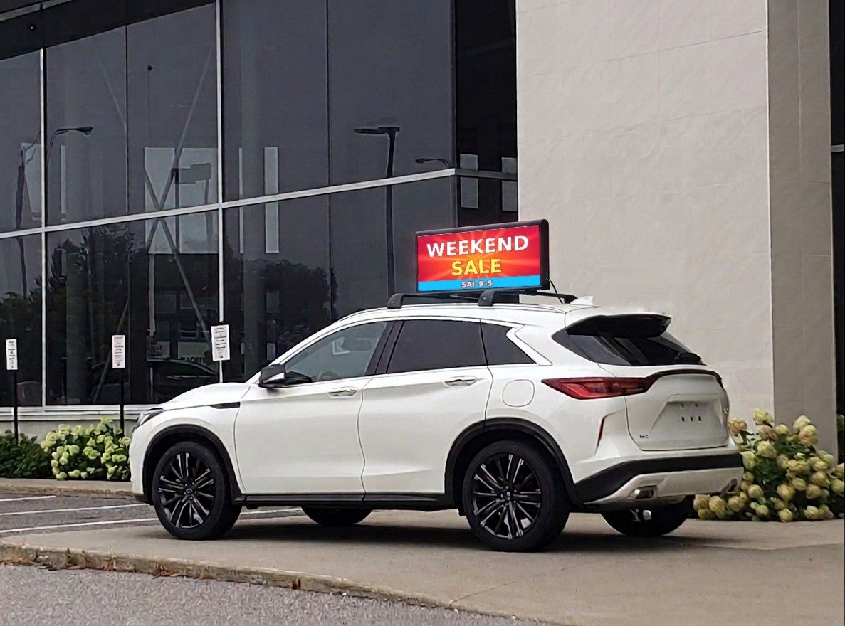 Double-sided LED screen on the roof of a white SUV parked in front of a dealership