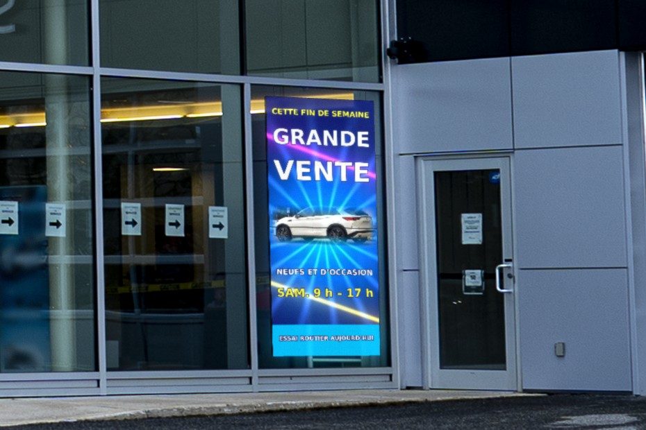 Écran DEL suspendu derrière la vitrine d’une concession automobile, face à la rue